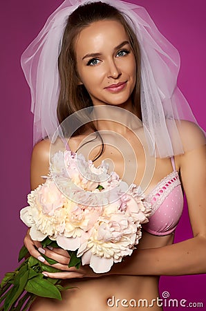 Beautiful sexy bride with long dark hair in a white veil, pink lace lingerie with bouquet of pale pink peonies with a gentle