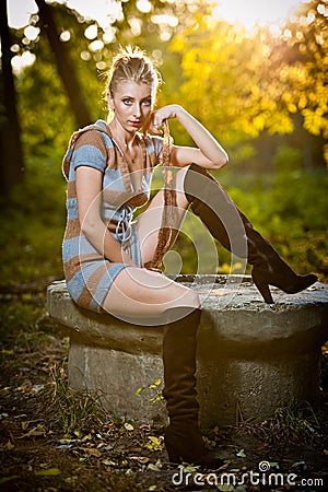 Beautiful sexy girl with long leather boots and short dress posing in park in autumn day.