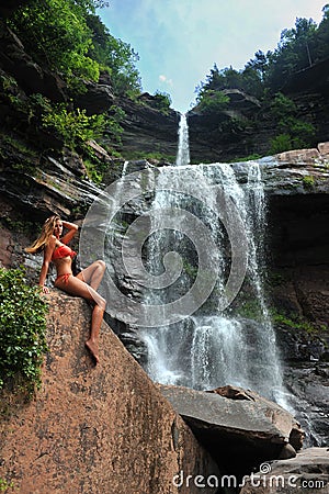 Beautiful slim fitness model posing sexy in front of waterfalls