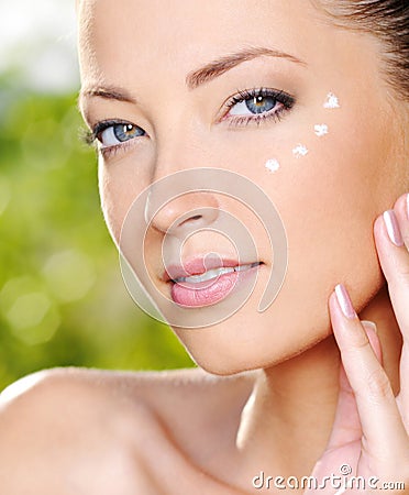 Beautiful woman applying cream near eyes