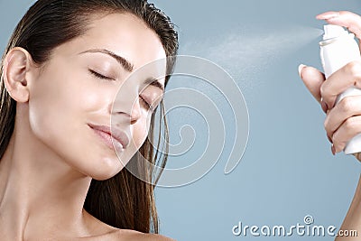Beautiful woman applying spray water treatment on face
