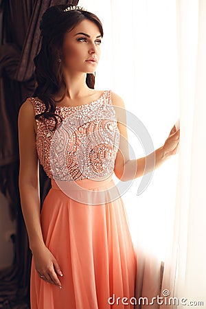 Beautiful woman with dark hair in elegant coral dress with diadem