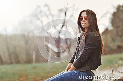 Beautiful woman in jacket and jeans sitting in a park