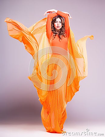 Beautiful woman in long orange dress posing dramatic in the studio