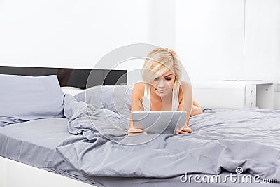 Beautiful woman lying on bed using digital tablet