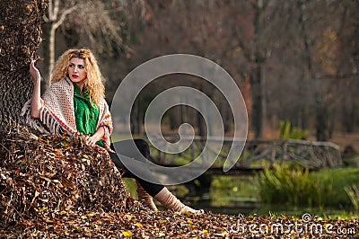 Beautiful woman posing in park during autumn season. Blonde girl wearing green blouse and big shawl posing outdoor. Long fair hair