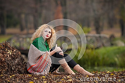 Beautiful woman posing in park during autumn season. Blonde girl wearing green blouse and big shawl posing outdoor. Long fair hair