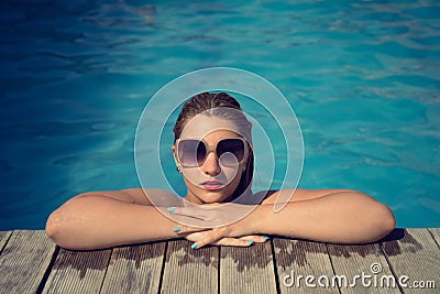 Beautiful woman relaxing at the poolside with wet hair wearing sunglasses