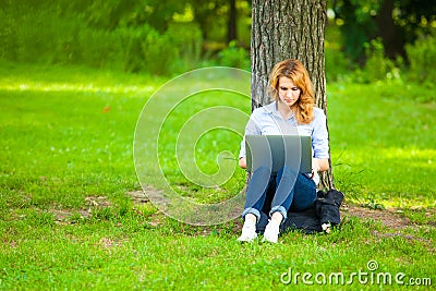 Beautiful woman sitting in park with laptop