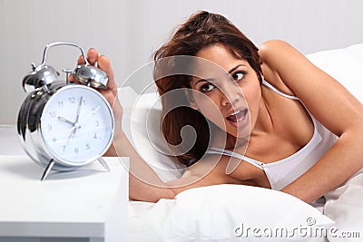 Beautiful woman waking up reaching for alarm clock