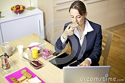 Beautiful woman working at home with computer during breakfast