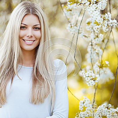 Beautiful young blonde woman standing near the apple tree