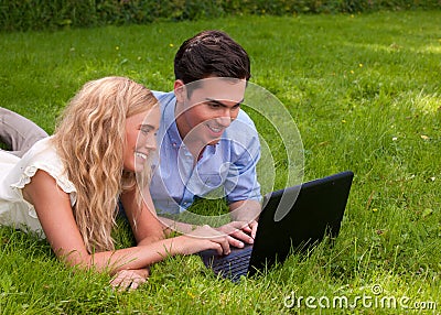 Beautiful, young couple with laptop in the grass