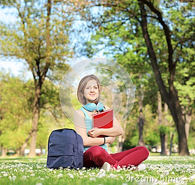 Beautiful young female student with book and headphones sitting