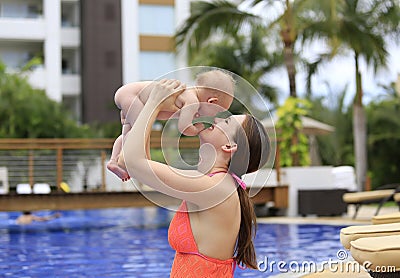 Beautiful young mother is holding baby girl outside near pool.