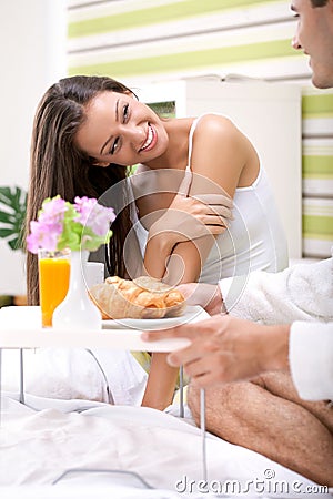 Beautiful young woman in bed with her husband serving breakfast