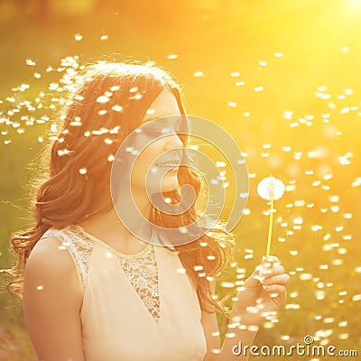 Beautiful young woman blowing dandelion. Trendy young girl at s