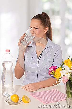 Beautiful young woman drinking a glass of water witth lemon
