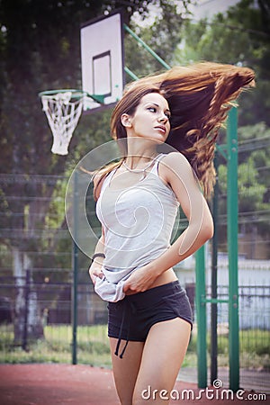 Beautiful young woman with fluttering hair playing basketball outdoors