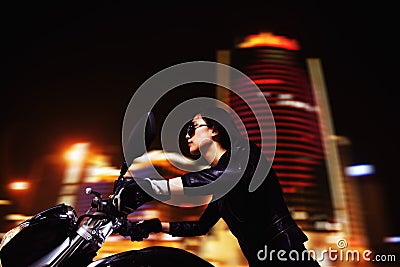 Beautiful young woman riding motorcycle in sunglasses through the city streets at night