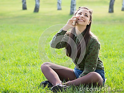 Beautyful girl talking on the phone sitting on the fresh grass
