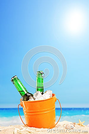 Beer bottles in a bucket of ice in the sand on a beach