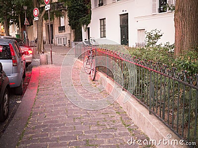 Bicycle leaning against iron fence, bathed in red light from traffic, Montmartre, Paris, early evening