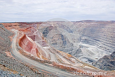 Big mine pit with little dump trucks and reddish soil