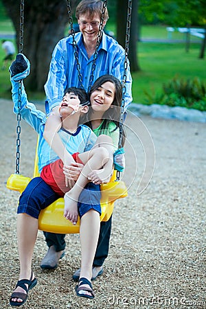 Big sister holding disabled brother on special needs swing at pl