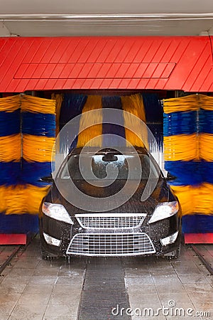 Black car in automatic car wash, rotating blue and yellow brushe