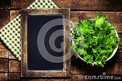 Black chalkboard for menu and fresh salad over wooden background