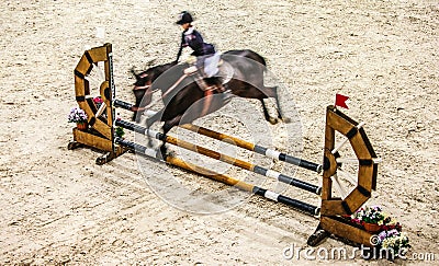 Black horse with rider jumping over obstacle. Riding competition.