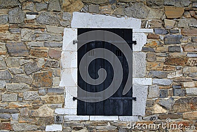 Black shuttered window in stone wall of building
