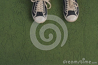 Black sneakers on a green welcome mat