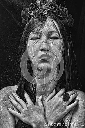 Black and white photo of a woman with roses on her head, arms crossed under the water jets