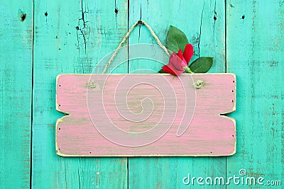 Blank pink weathered sign with red flower hanging on antique green wood door