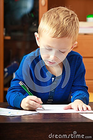 Blond boy child kid with pen writing on piece of paper. At home.