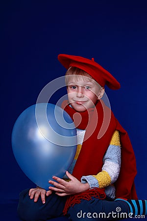 Blond boy in red scarf smiling with blue balloon