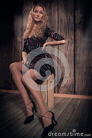 Blond curly hair lady sitting in a pose on the box over wooden wall background