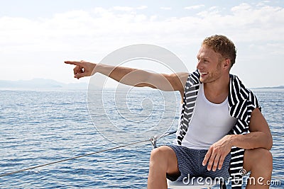 Blond handsome young man on a sailing boat pointing at something