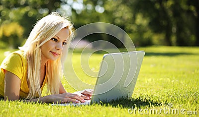 Blonde Girl with Laptop. Smiling Beautiful Woman Lying on Grass