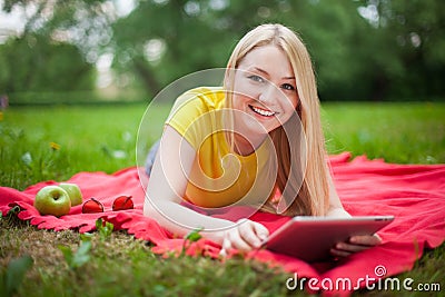 Blonde girl lying in the park with tablet