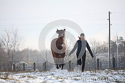Blonde teenager girl and brown horse running in the snow