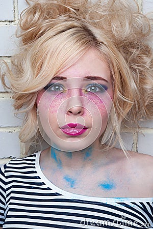 Blonde woman with bright creative make-up near the wall