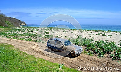 Blue car covered in mud on dirt road to a beach