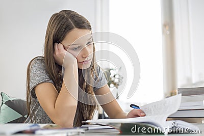 Bored girl studying at table in house