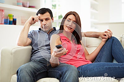 Bored Husband With Wife On Sofa Watching TV