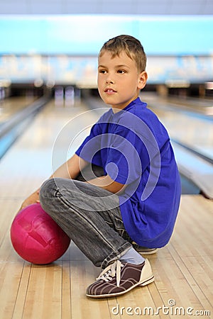 Boy with ball sits on floor in bowling