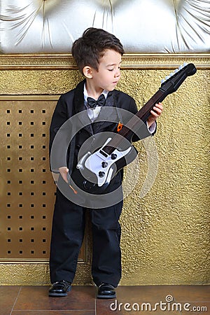 Boy in black tuxedo stands with guitar