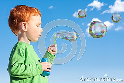 Boy child blowing soap bubbles into sky